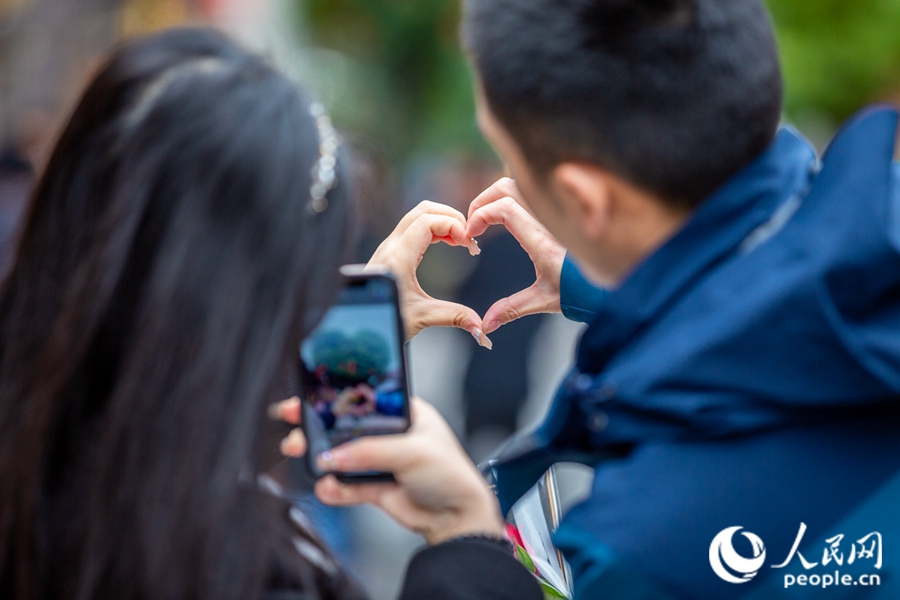 年輕情侶比心“打卡”?？道跀z