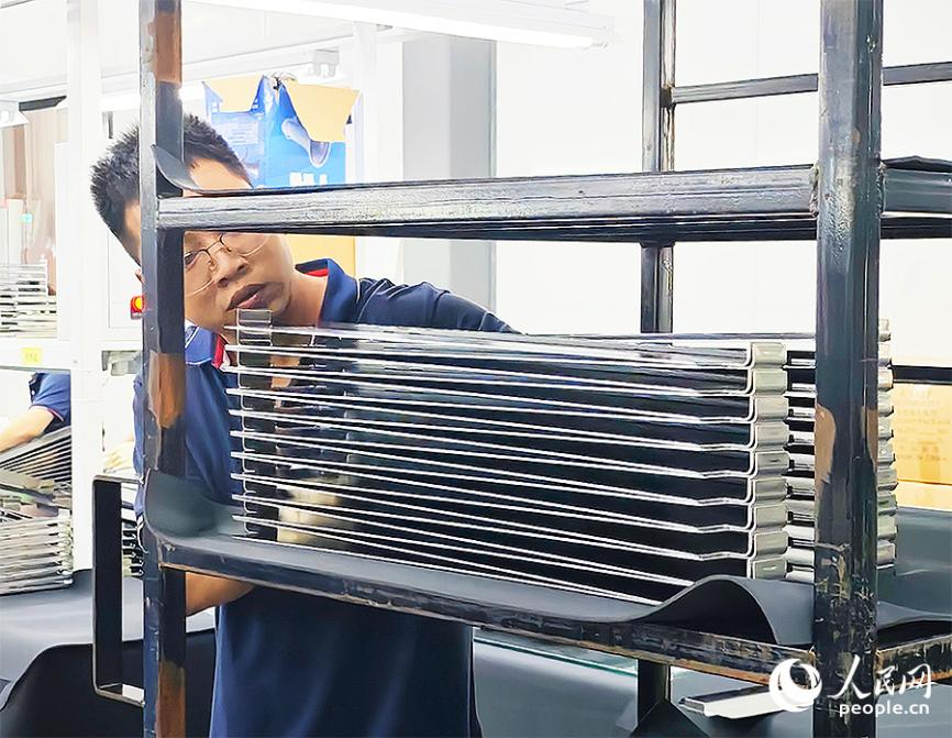 東恒新能源集團(tuán)廠房?jī)?nèi)，一名工作人員正將經(jīng)過(guò)質(zhì)檢的新能源汽車電池模組側(cè)板整齊碼放到貨架上。人民網(wǎng) 黃東儀攝