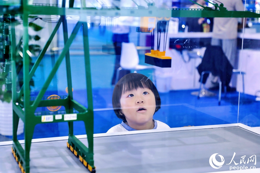 小朋友端詳岸邊集裝箱起重機設(shè)備模型。人民網(wǎng) 李唯一攝