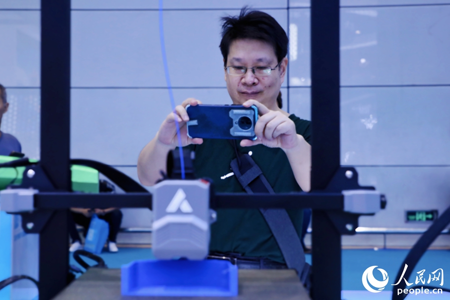 觀眾饒有興趣地用手機拍攝正在運行的3D打印設(shè)備。人民網(wǎng) 李唯一攝