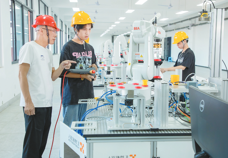 全國(guó)先進(jìn)工作者林福(左)指導(dǎo)學(xué)生操作工業(yè)機(jī)器人
